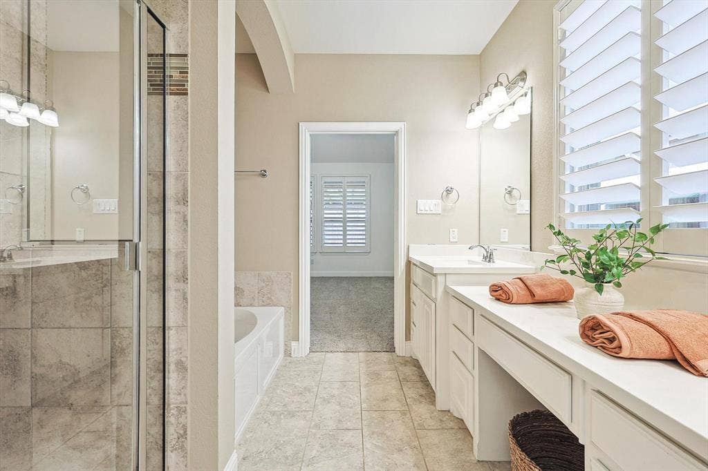 Dual vanity with integrated sinks, white cabinetry, a built-in makeup counter, a frameless glass shower enclosure, and a built-in soaking tub