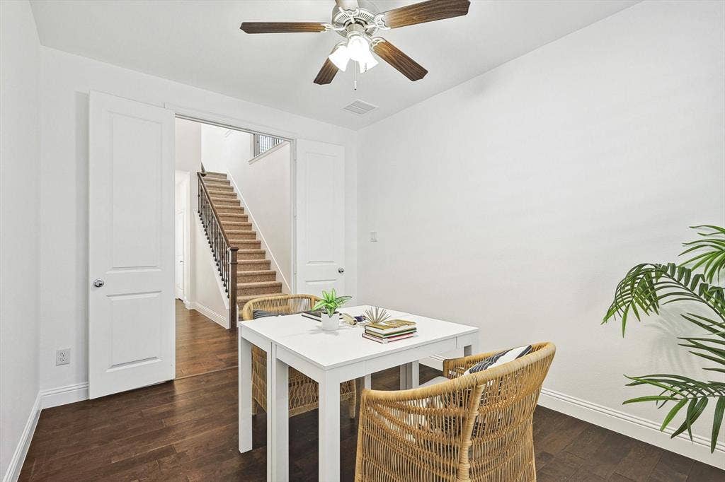 Wood-finish flooring with white baseboards, a ceiling fan with light fixture, and white interior walls