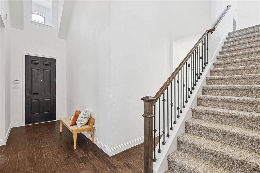 Foyer featuring wood-finish flooring, a paneled entry door, a multi-story wall with an upper window, and a carpeted staircase with a wrought iron and wood balustrade