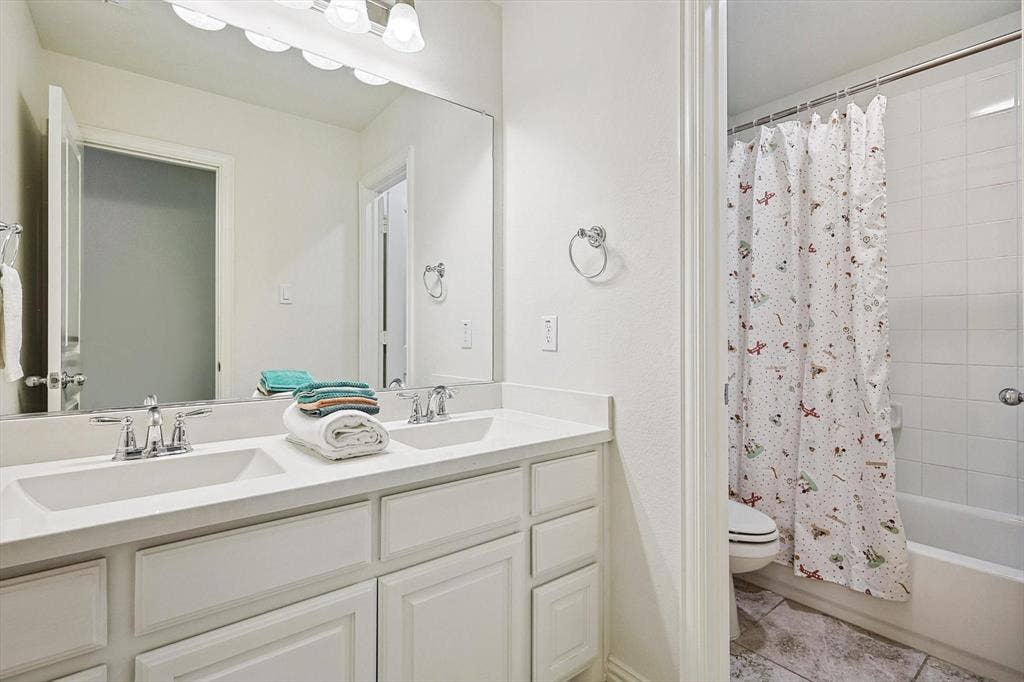 Double vanity with integrated sinks, white cabinetry, chrome fixtures, large wall-mounted mirror, and tile flooring