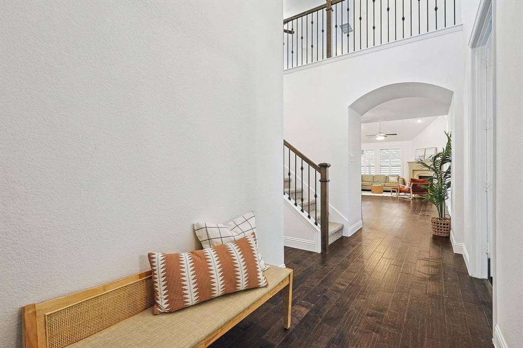 Hardwood-finish flooring, staircase with wrought iron balusters, arched entryway, and a second-story landing
