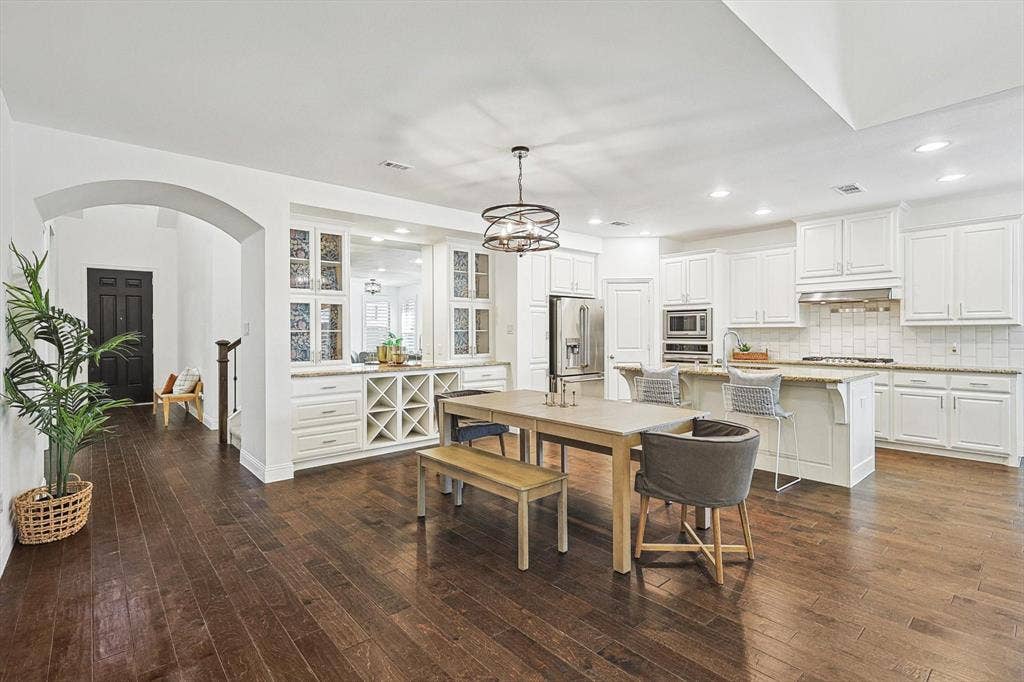 Hardwood flooring throughout, white cabinetry with integrated wine storage, stainless steel appliances, kitchen island with counter seating, and recessed lighting