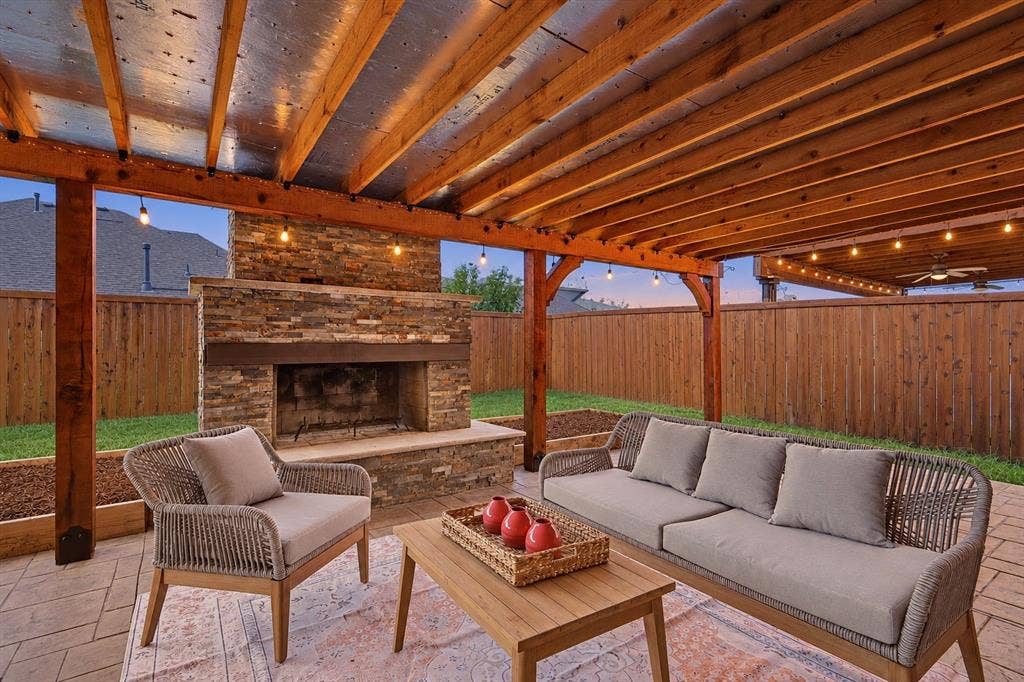 Expansive covered patio featuring a stone-clad fireplace, wood pergola, string lighting, and paver flooring *virtual twilight added