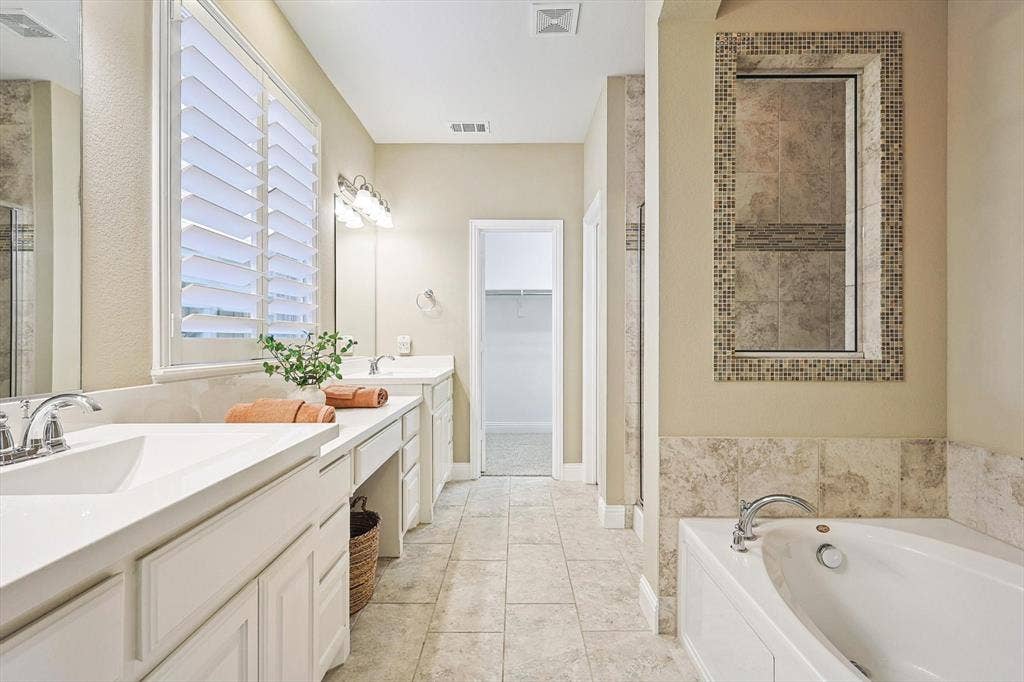 Dual vanities with integrated sinks, white cabinetry, a built-in soaking tub, and tile flooring