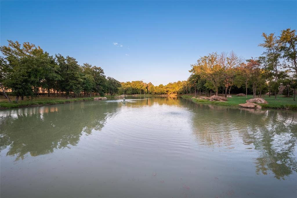 Expansive water feature with a central fountain, bordered by a manicured lawn and mature trees