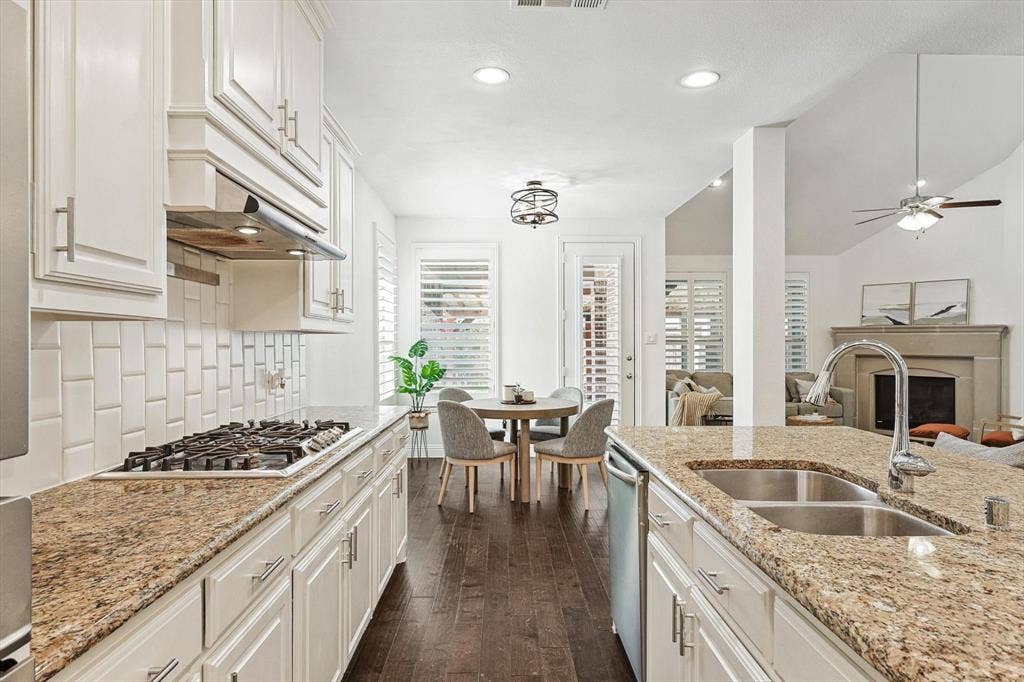 Kitchen featuring white cabinetry, granite countertops, a gas range, subway tile backsplash, and a double basin sink with a high-arc faucet