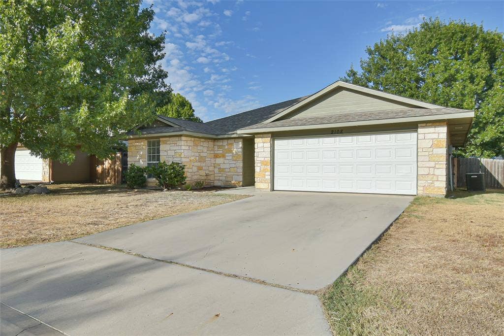 2108 8th Street, Brownwood, TX 76801 Stone-clad exterior, attached two-car garage, concrete driveway, and mature landscaping