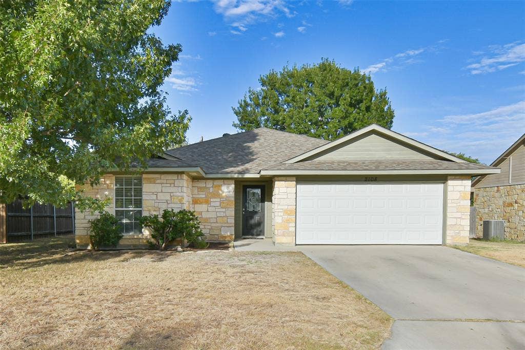 2108 8th Street, Brownwood, TX 76801 Stone veneer exterior with a composition shingle roof, attached garage, and concrete driveway