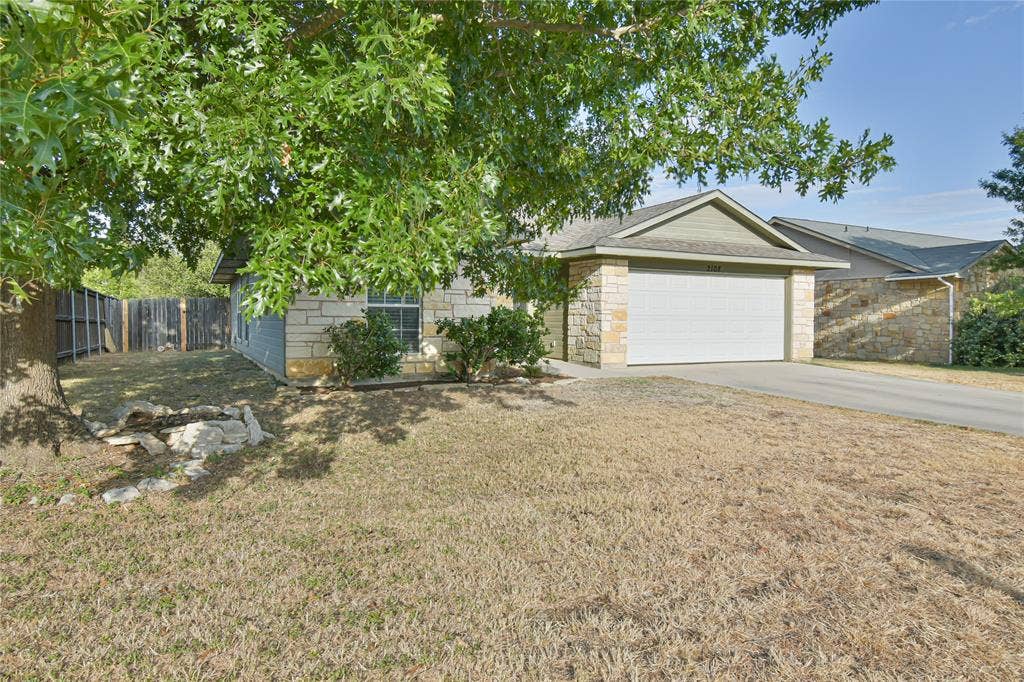 2108 8th Street, Brownwood, TX 76801 Stone facade with a single-car garage, mature trees, and a fenced side yard