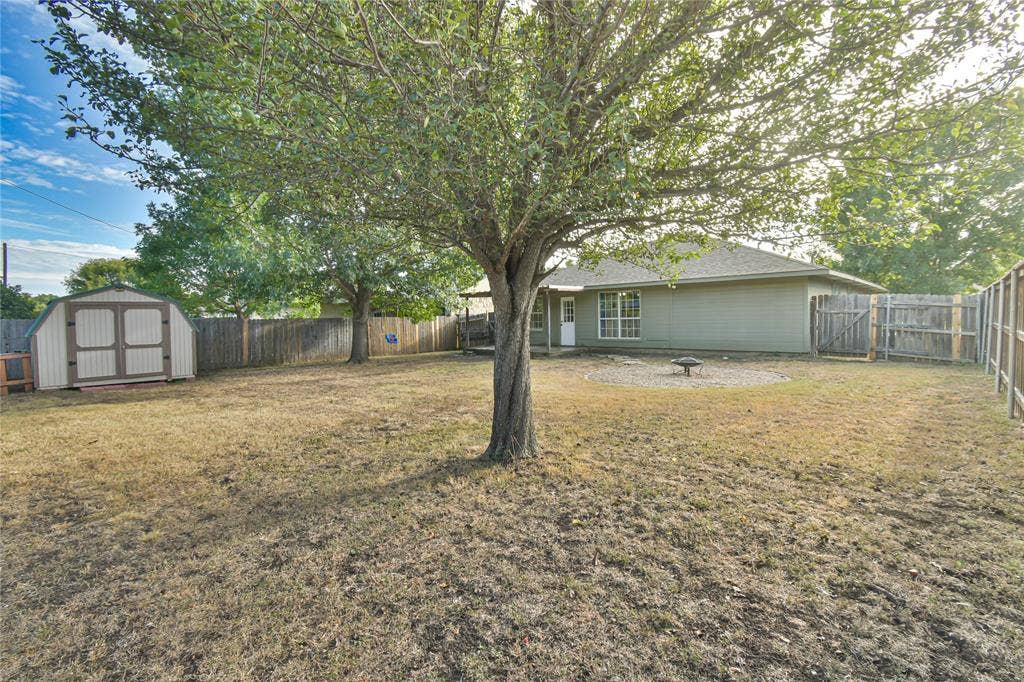 2108 8th Street, Brownwood, TX 76801 Expansive rear yard featuring a privacy fence, mature trees, and an outdoor storage shed