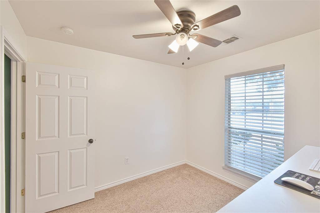 2108 8th Street, Brownwood, TX 76801 Neutral wall paint, textured carpeting, window with blinds, ceiling fan with integrated lighting, and a paneled interior door