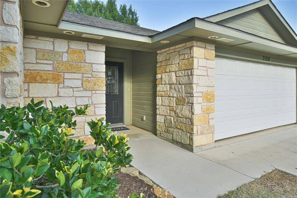 2108 8th Street, Brownwood, TX 76801 Stone veneer facade, recessed lighting, covered entry, front door with decorative glass, and a paneled garage door