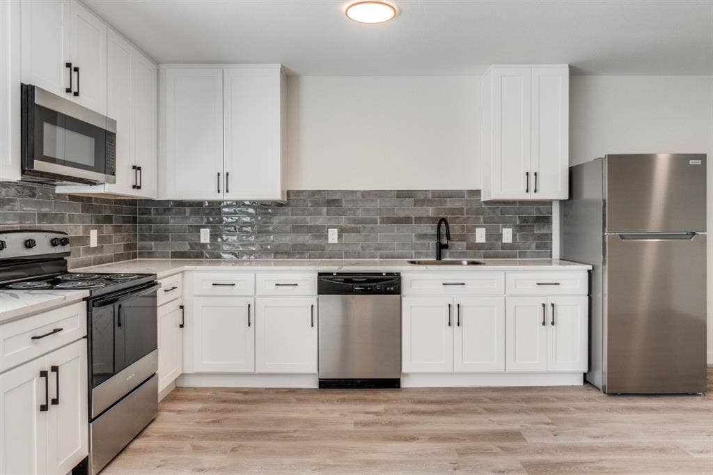 5917 Gaston Avenue, #115, Dallas, TX 75214 Kitchen featuring white cabinetry, stainless steel appliances, dark subway tile backsplash, light countertops, and wood-finish flooring