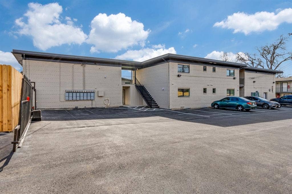 5917 Gaston Avenue, #115, Dallas, TX 75214 Paved parking lot with designated spaces, featuring a light-colored brick exterior and dark framed windows