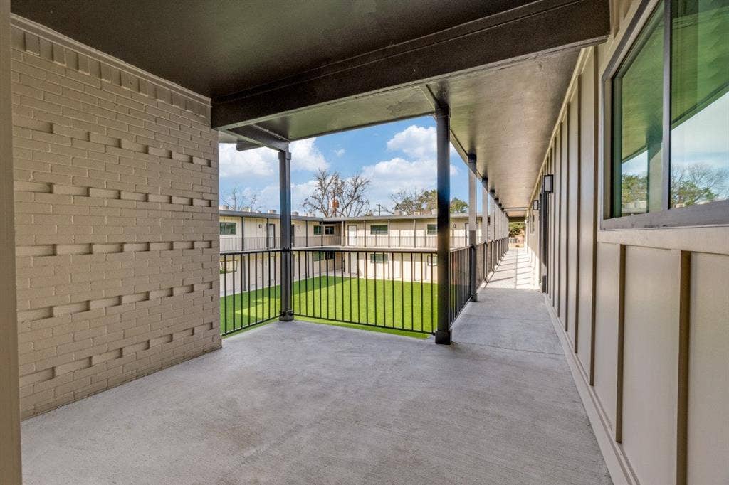 5917 Gaston Avenue, #115, Dallas, TX 75214 Concrete balcony with black metal railings, textured brick wall, and board and batten siding