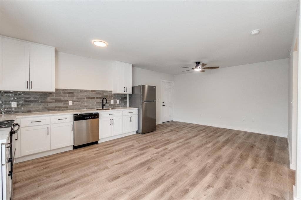 5917 Gaston Avenue, #115, Dallas, TX 75214 Kitchen featuring white cabinetry, stainless steel appliances, a tile backsplash, and light wood-finish flooring