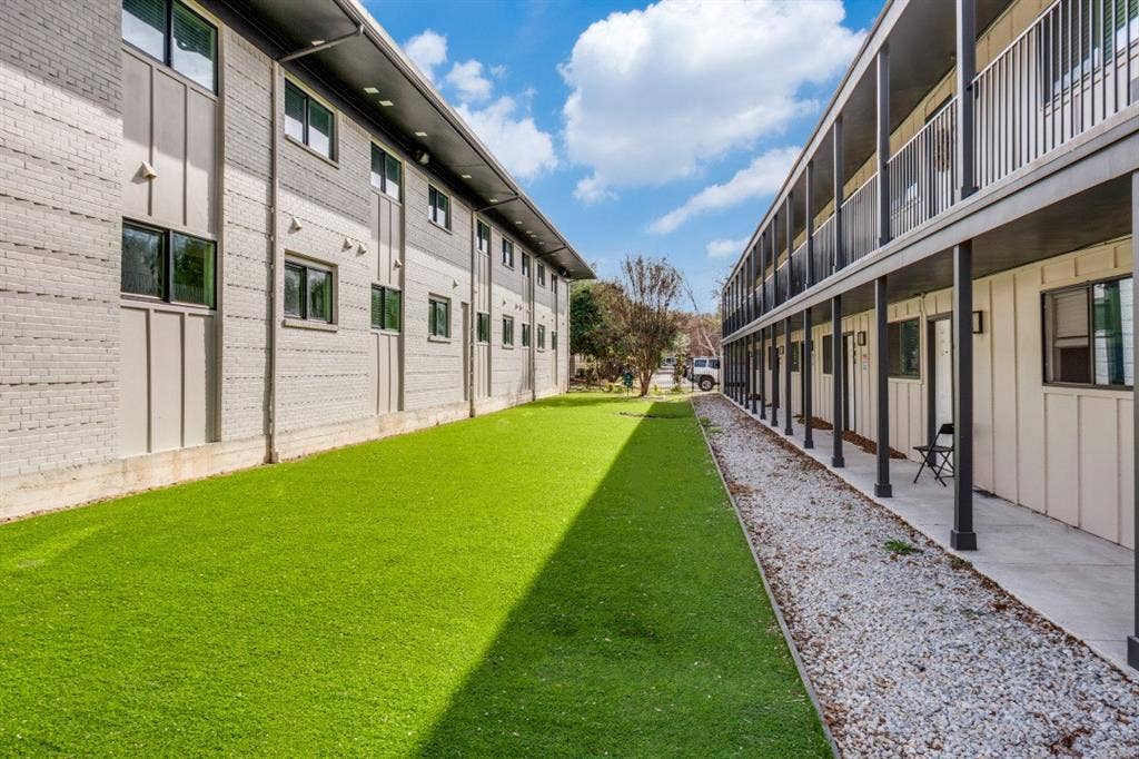 5917 Gaston Avenue, #115, Dallas, TX 75214 Outdoor space featuring a synthetic turf lawn, gravel pathway, brick facade, and multi-level balconies with metal railings