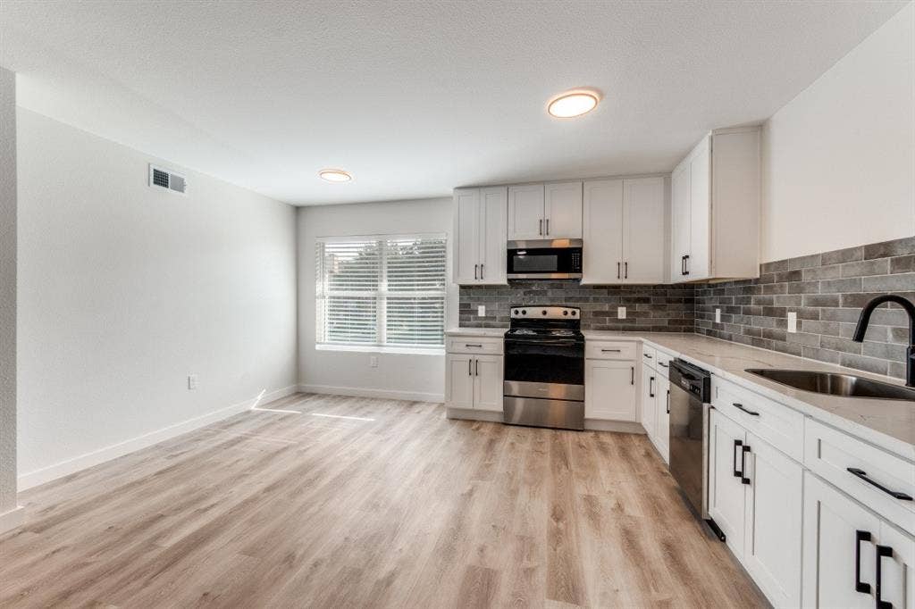 5917 Gaston Avenue, #115, Dallas, TX 75214 Open-concept kitchen with wood-finish flooring, white cabinetry, stainless steel appliances, and a subway tile backsplash