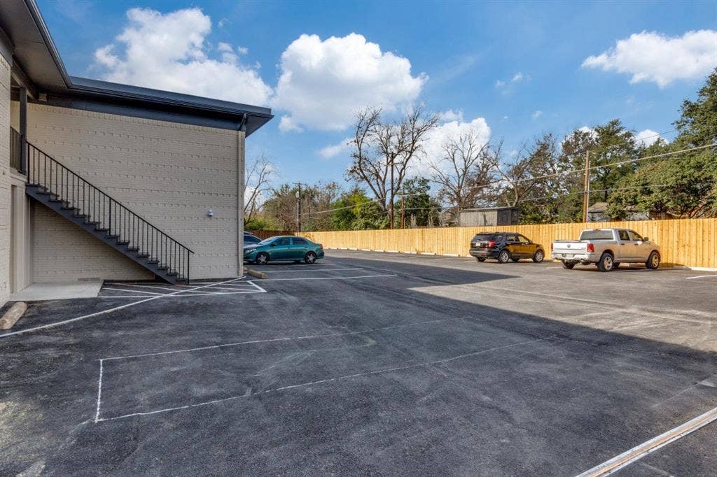 5917 Gaston Avenue, #115, Dallas, TX 75214 Paved parking area, exterior stairwell with black metal railings, and a wood privacy fence