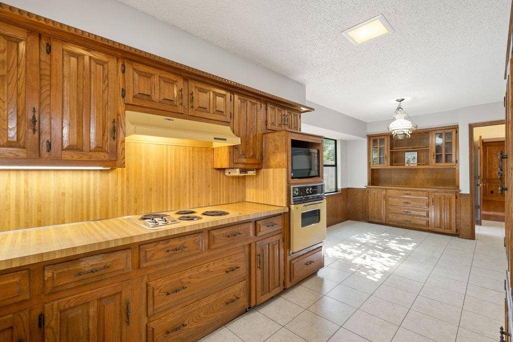Extensive wood cabinetry, built-in wall oven and microwave, integrated cooktop, tile flooring, and a decorative pendant light fixture