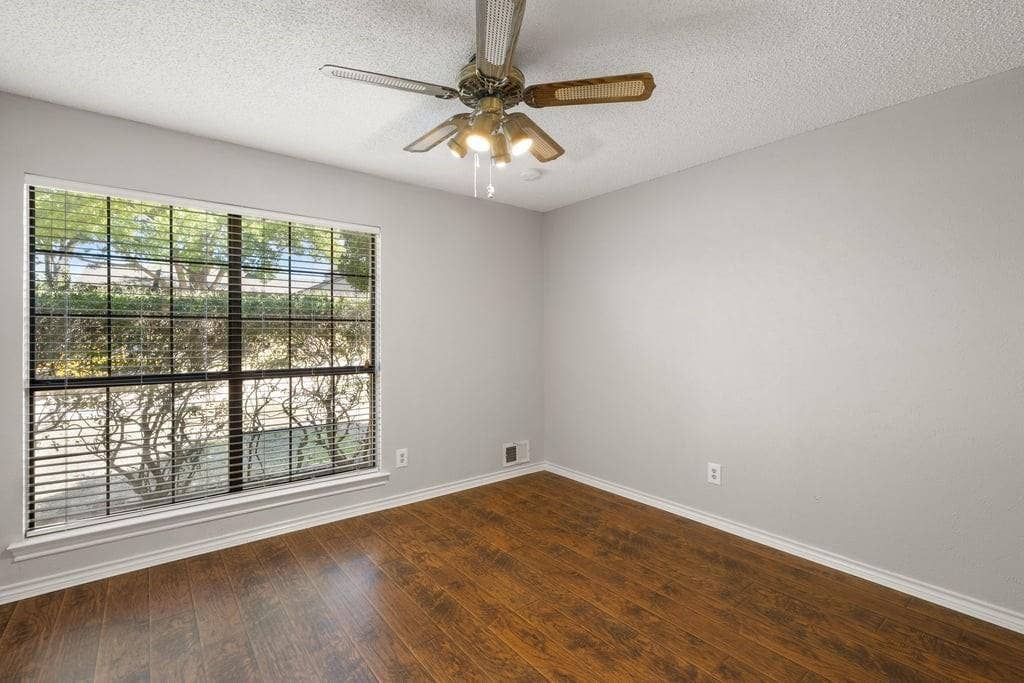 Room featuring wood-finish flooring, a ceiling fan with integrated lighting, and a window with blinds