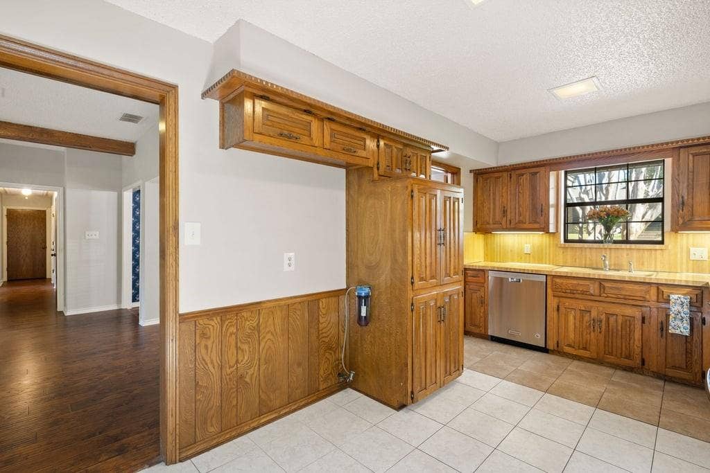 Kitchen featuring wood-finish cabinetry, stainless steel dishwasher, tile flooring, and a large window