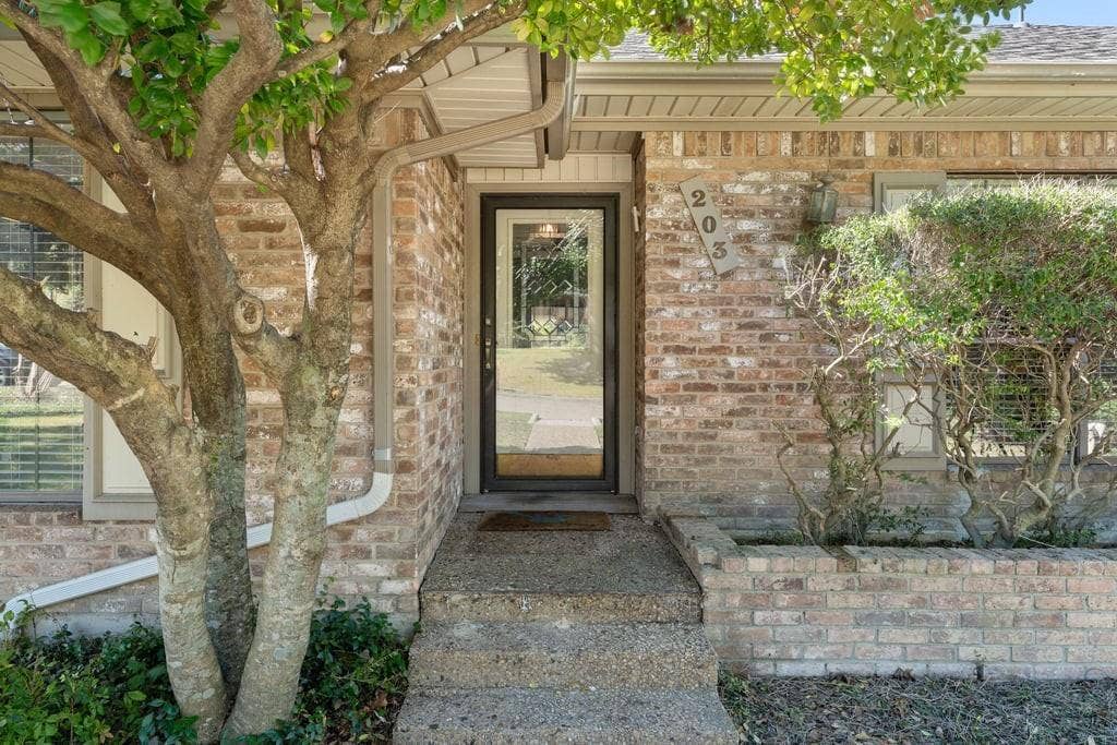 Brick facade with a full-light entry door, concrete steps, and integrated brick planter