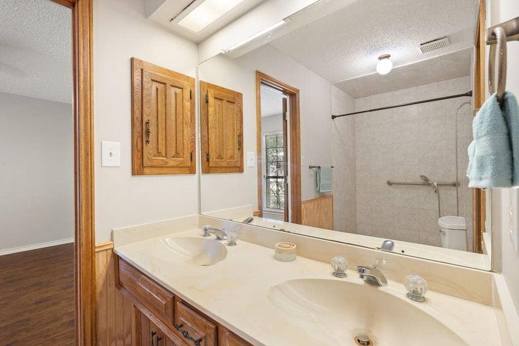 Dual sinks set in a light-toned countertop, wood-finish cabinetry, and a mirrored wall