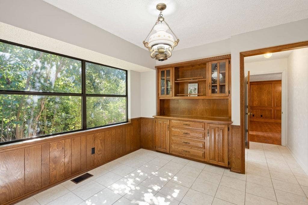 Extensive window with black framing, wood-paneled wainscoting, built-in wood cabinetry with glass door accents, and tile flooring