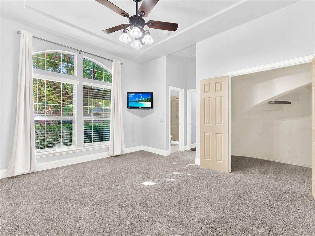 10222 Plainsman Lane, Frisco, TX 75035 Arched window with blinds, ceiling fan with light fixture, tray ceiling, wall-mounted television, and carpeted flooring