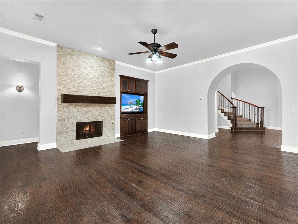 10222 Plainsman Lane, Frisco, TX 75035 Stacked stone fireplace with a wood-beam mantel, built-in media cabinetry, wood-finish flooring, and an arched entryway