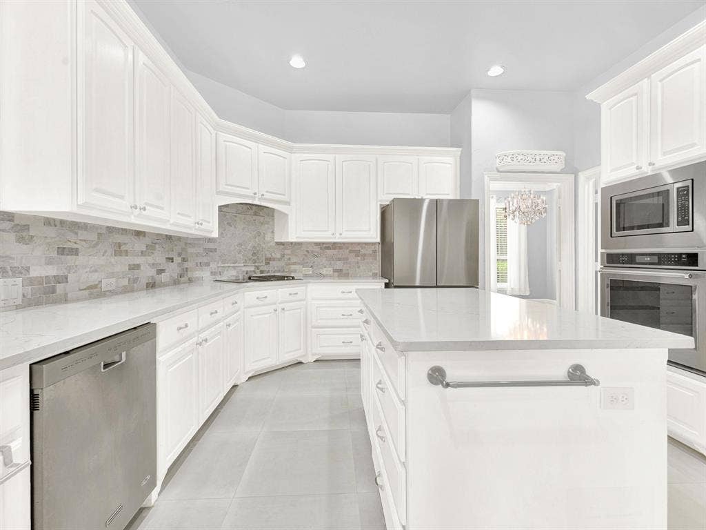 10222 Plainsman Lane, Frisco, TX 75035 White cabinetry with hardware, light-toned countertops, a tile backsplash, stainless steel appliances, and a central island