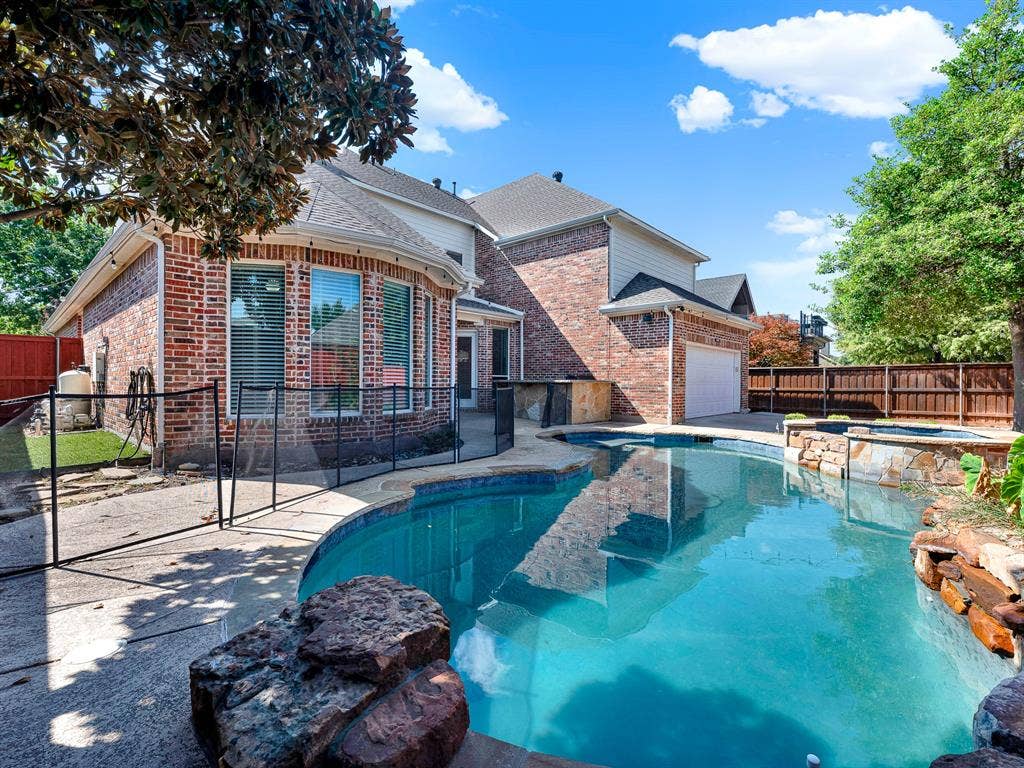 10222 Plainsman Lane, Frisco, TX 75035 Brick exterior with a multi-level roofline, featuring a built-in swimming pool, integrated spa, and an outdoor kitchen area