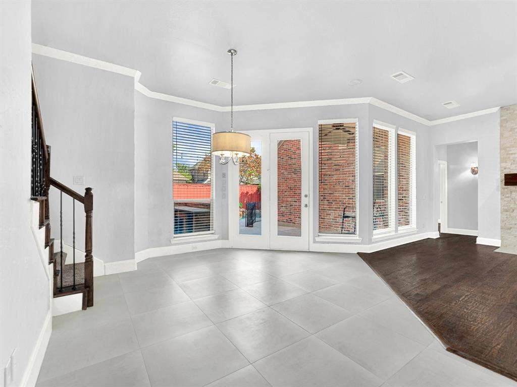 10222 Plainsman Lane, Frisco, TX 75035 Bay window feature with multiple panes, light gray tile flooring, French doors, wood-finish flooring, and a built-in staircase with dark wood and wrought iron balusters