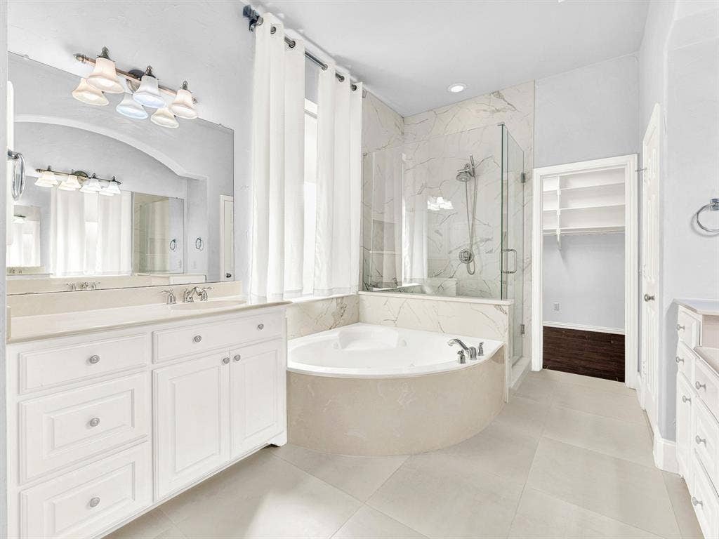 10222 Plainsman Lane, Frisco, TX 75035 Spacious bathroom featuring a built-in jetted tub, glass-enclosed shower, dual vanities with integrated sinks, and neutral tile flooring