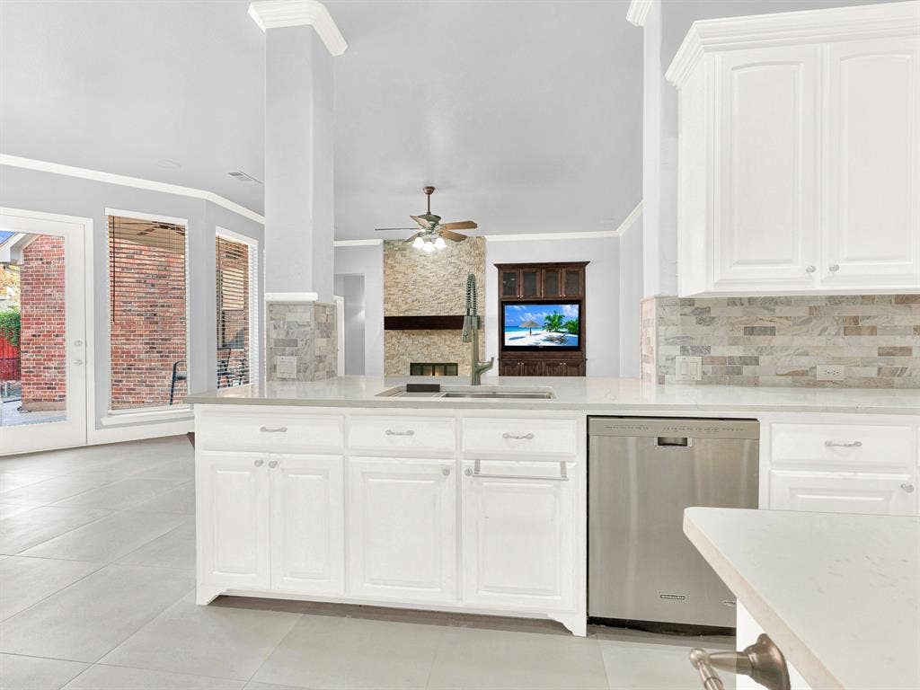 10222 Plainsman Lane, Frisco, TX 75035 White cabinetry, light countertops, subway tile backsplash, stainless steel dishwasher, and a centered island sink with a gooseneck faucet
