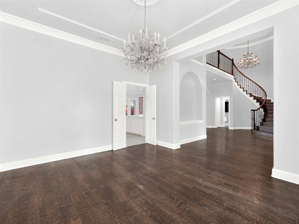 10222 Plainsman Lane, Frisco, TX 75035 Dark wood-finish flooring, two crystal chandeliers, a grand curved staircase with wood railing, white crown molding, and an arched entryway