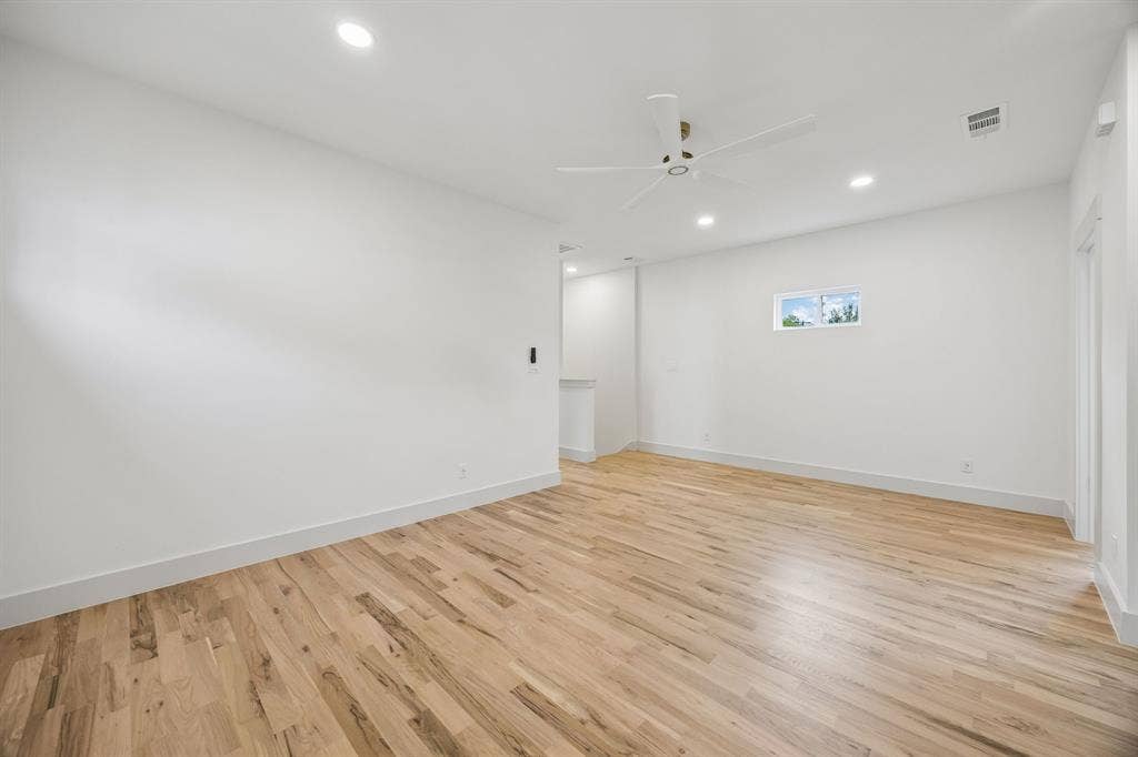 Recessed lighting and a ceiling fan illuminate a spacious room with wood-finish flooring