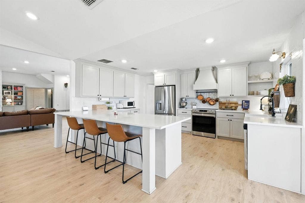 185 Quail Run Court, Decatur, TX 76234 Open-concept kitchen featuring an expansive island with seating, stainless steel appliances, white cabinetry, and wood-finish flooring