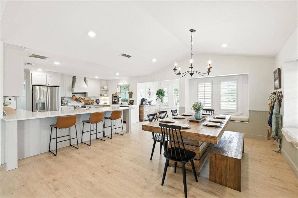 185 Quail Run Court, Decatur, TX 76234 Light wood-finish flooring, vaulted ceiling, white kitchen cabinetry with stainless steel appliances, breakfast bar with pendant lighting, and a dining area with a chandelier and window seating