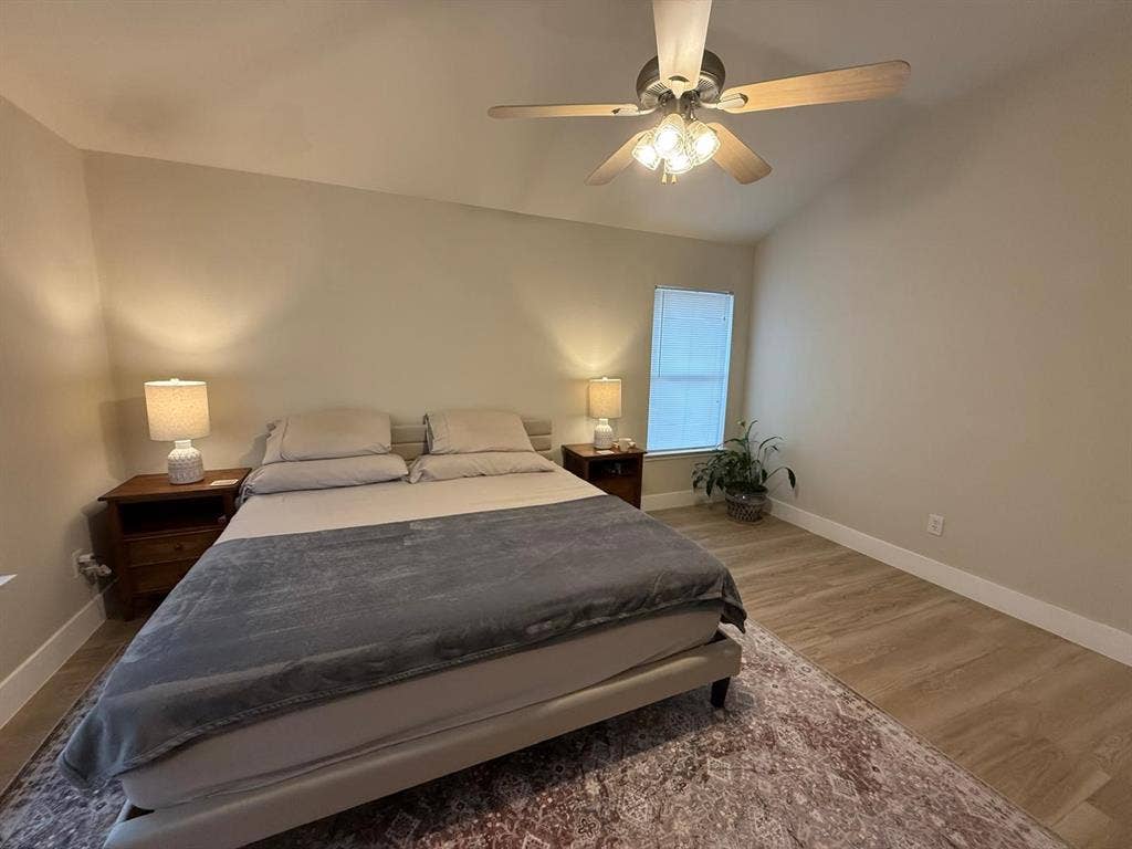 Vaulted ceiling with a ceiling fan, wood-finish flooring, and a single window with blinds