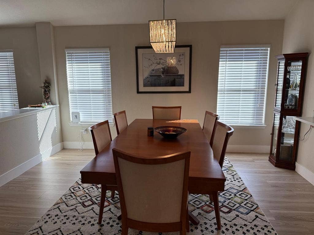 Recessed wall detail, three windows with blinds, wood-finish flooring, and a contemporary chandelier