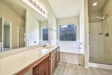 Wood-finish flooring, built-in soaking tub, separate glass-enclosed shower, single vanity with integrated sink, and large wall-mounted mirror