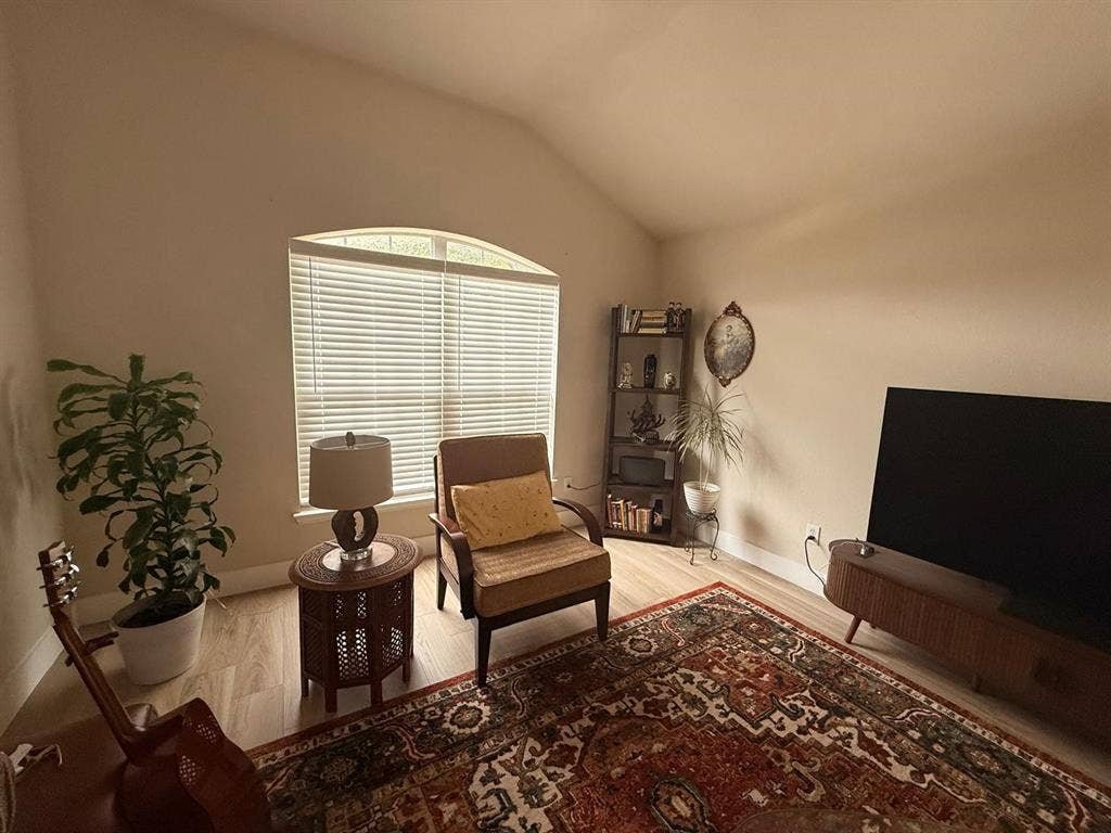 Vaulted ceiling, arched window, wood-finish flooring, and neutral wall tones
