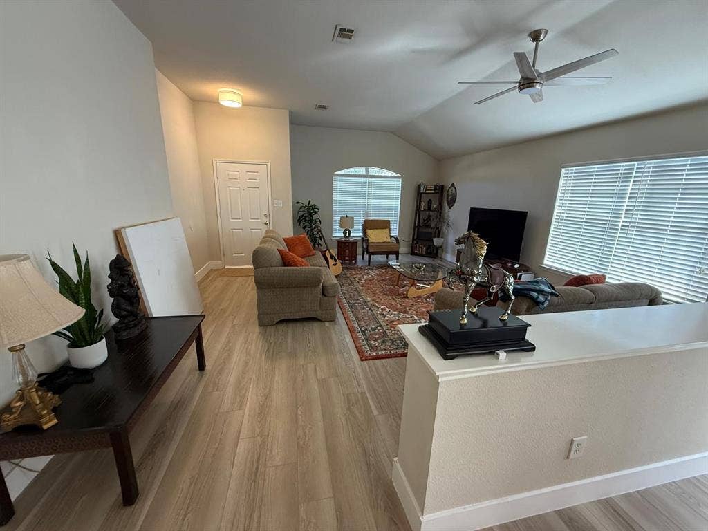Vaulted ceilings with a ceiling fan, wood-finish flooring, and multiple windows