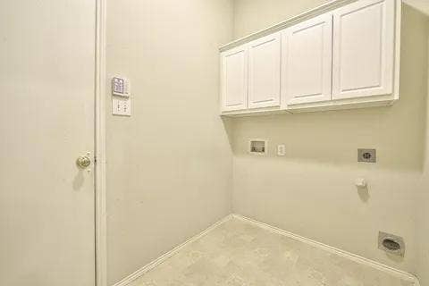 White cabinetry with crown molding, wall-mounted electrical outlets, and a utility hookup