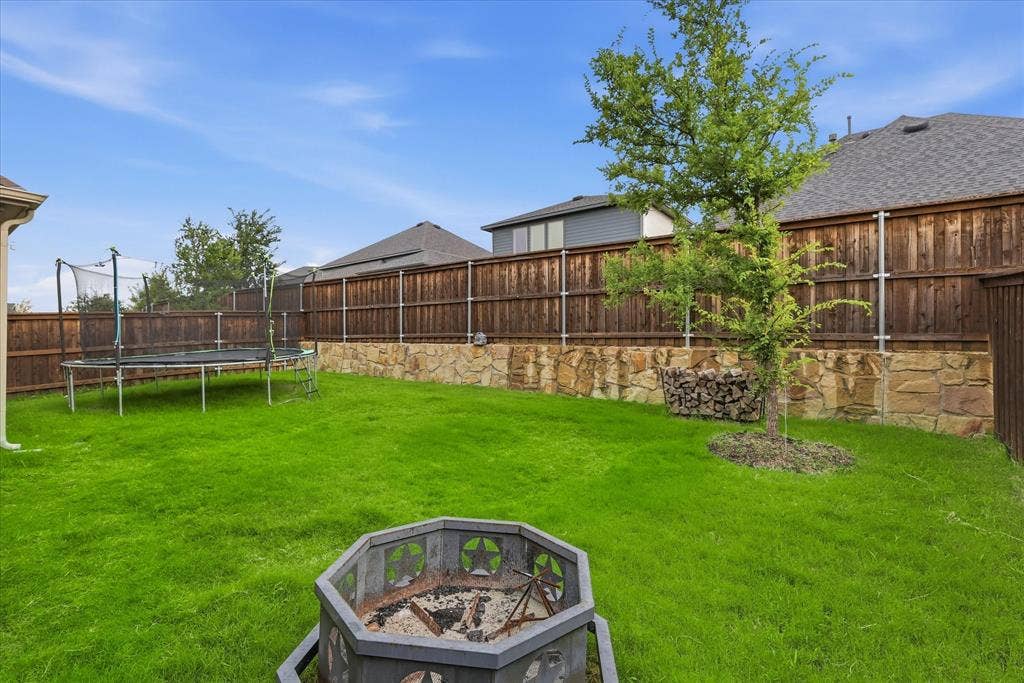2637 Basswood Drive, Northlake, TX 76226 Expansive backyard featuring a manicured lawn, wood privacy fencing, stone retaining wall, and a fire pit