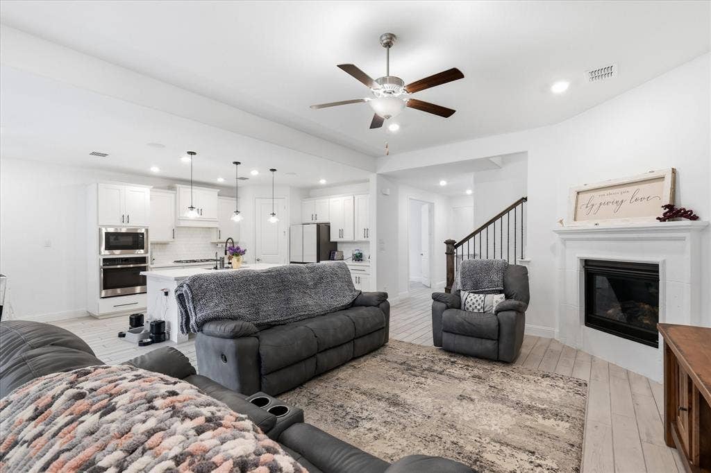 2637 Basswood Drive, Northlake, TX 76226 Open-concept living area featuring light wood-finish flooring, a contemporary ceiling fan, and a fireplace with a white mantel