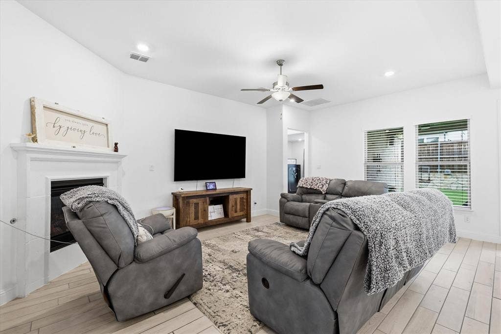 2637 Basswood Drive, Northlake, TX 76226 White walls with recessed lighting, a fireplace with a white mantel, a ceiling fan, multiple windows with blinds, and wood-finish flooring
