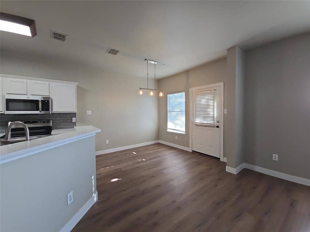 8621 Brunswick Drive, Plano, TX 75024 White shaker cabinetry, stainless steel appliances, grey subway tile backsplash, wood-finish flooring, and a contemporary chandelier